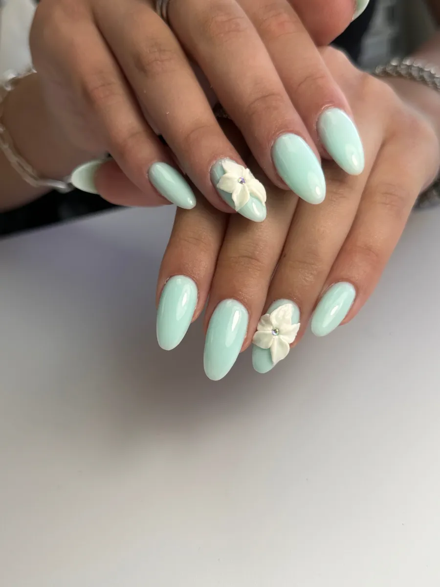 Uñas almendradas color menta con flores blancas esculpidas en 3D y cristales